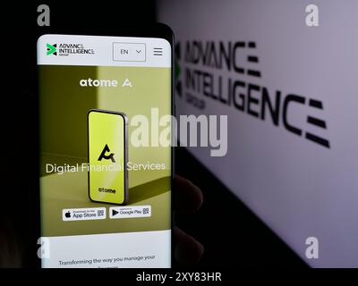 Persona che possiede uno smartphone con pagina Web dell'azienda Fintech di Singapore Advance Intelligence Group con logo. Messa a fuoco al centro del display del telefono. Foto Stock