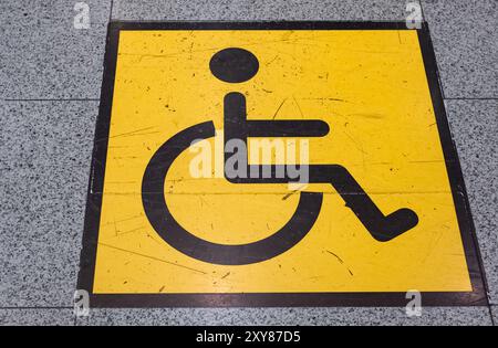 Cartello di accesso per disabili dipinto di giallo e nero sul pavimento. Simbolo della sedia a rotelle sul pavimento per il parcheggio per disabili. Strada per sedie a rotelle Foto Stock