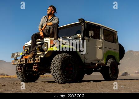 Uomo che visita il vulcano Bromo in jeep e siede sul cofano dell'auto, Java, Indonesia Foto Stock