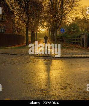 Uomo che cammina nel tramonto dorato su una strada acciottolata che getta una lunga ombra Foto Stock