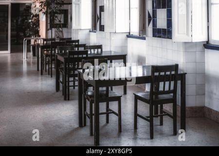 Interni vuoti di un caffè minimalista con tavoli e sedie in legno nero disposti in file contro una parete piastrellata con motivi blu e bianchi. Lo spazio Foto Stock