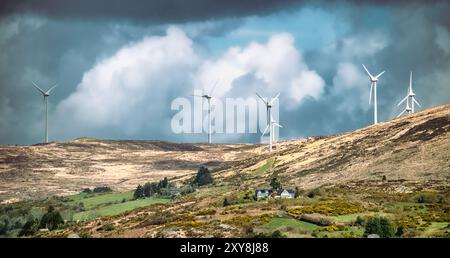 Poche turbine eoliche sono alte su una collina, catturando l'energia del vento sotto un cielo nuvoloso. Foto Stock