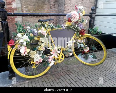 Bicicletta gialla decorata con fiori in un canale di Gouda, Paesi Bassi Foto Stock