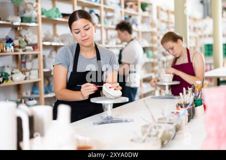 Giovane donna che dipinge la tazza di ceramica in laboratorio di ceramica Foto Stock