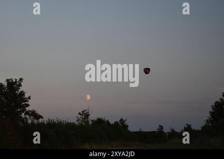 Mongolfiera che vola al crepuscolo con la luna che si alza. Foto Stock