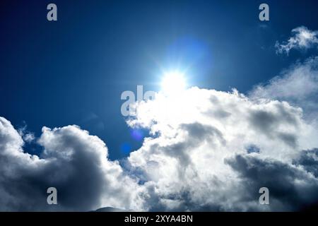 Cielo blu scuro con un brillante sole stellato che splende attraverso la nuvola scura e frastagliata di nimbus cumulus bordata di stelle bianche e piccole che sbirciano attraverso il da Foto Stock