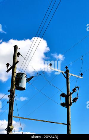 Doppi cavi telefonici in legno per telegrafo trasformatori e cavi in campagna contro il cielo blu profondo e un piccolo centro nuvola bianco Foto Stock