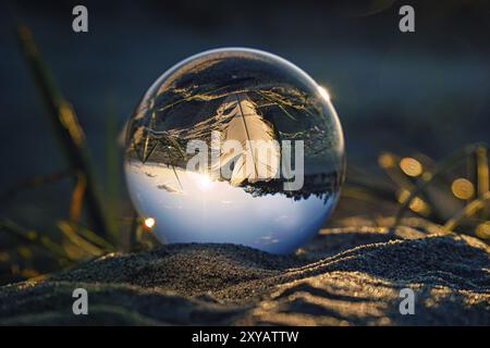 Palla di vetro sulla spiaggia del Mar Baltico a Zingst con una piuma raffigurata nella palla con il paesaggio. Il tramonto crea un'atmosfera calda e luminosa Foto Stock