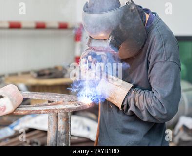 Gli operatori indossano caschi leggeri a regolazione automatica e guanti per la saldatura dell'acciaio in fabbrica. Foto Stock