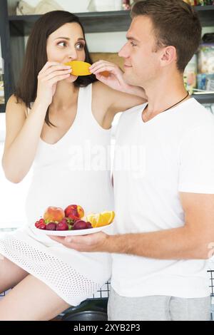 Giovane uomo e donna incinta con un piatto di frutta in kithen. La gravidanza e il concetto di nutrizione Foto Stock