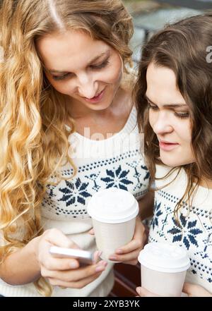 Due amiche donne felici che condividono i social media in uno smartphone all'aperto in città. Due giovani donne che guardano insieme il telefono cellulare mentre si distinguono Foto Stock