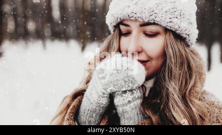 Bella giovane donna in neve fantasia bosco invernale. Ragazza che indossa morbidi guanti, cappuccio e cappotto. Foresta di Natale, alberi su sfondo sfocato. Incrociato Foto Stock