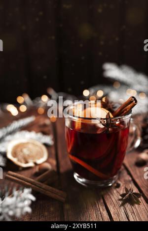 Foto di concetto del periodo di Natale. Tazza o tazza di vetro con VIN brulé all'interno su tavola di legno, sfondo. Ghirlande, decorazioni natalizie, cannella, hazelnu Foto Stock