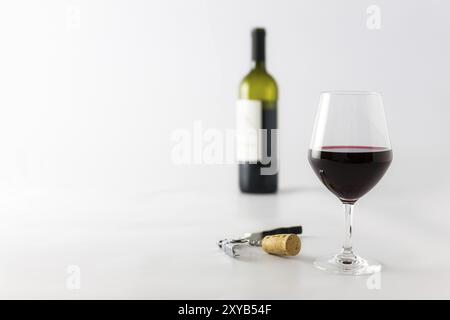 Bicchiere di vino rosso e bottiglia su uno sfondo bianco con sughero e cavatappi Foto Stock