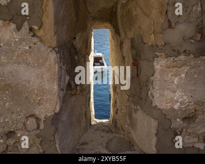 Una piccola finestra in un muro di pietra offre una vista di una barca nell'acqua blu, dubrovnik, Mar Mediterraneo, Croazia, Europa Foto Stock