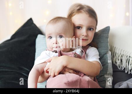 Stile di vita ritratto della cute ragazze caucasica sorelle holding piccolo bambino sul letto. Amore Familiare legare assieme concetto Foto Stock