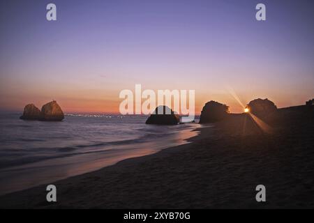 Tramonto nell'Algarve. L'orizzonte è formato dalla città illuminata di Lagos Foto Stock