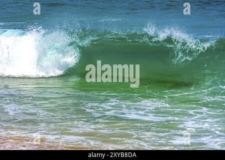 Piccola Onda con trasparenti acque verde la rottura sul bordo della spiaggia Foto Stock