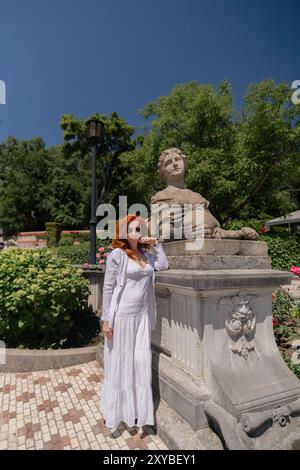 Una donna con un vestito bianco si trova di fronte a una statua Foto Stock