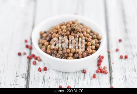 Grani di pepe rosa freschi (conservati) su un vecchio e rustico tavolo in legno, messa a fuoco selettiva, foto ravvicinata Foto Stock