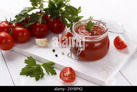 Salsa di pomodoro fatta in casa con aglio prezzemolo, pepe bianco e nero in un primo piano bianco. Orizzontale Foto Stock