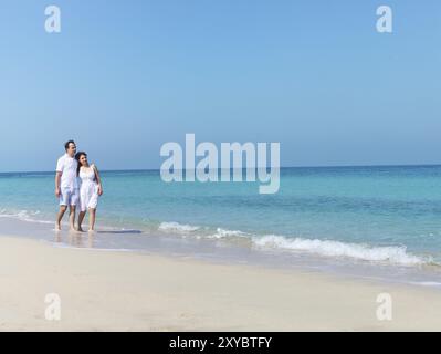 Giovane coppia felice di camminare sulla spiaggia sorridente holding attorno a ciascun altro Foto Stock