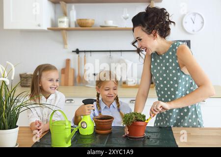 Bella giovani donne con due piccole figlie carino piantare fiori in vaso in cucina Foto Stock