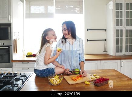 Bellissima bambina con la madre in cucina preparare una macedonia di frutta fresca in cucina Foto Stock