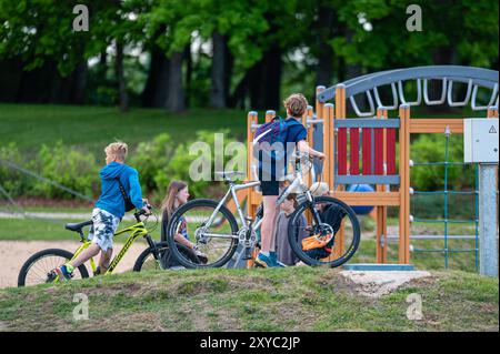 Aluksne, Lettonia - 24 maggio. 2023: I bambini pedalano in bicicletta e giocano in un parco in un pomeriggio di sole Foto Stock