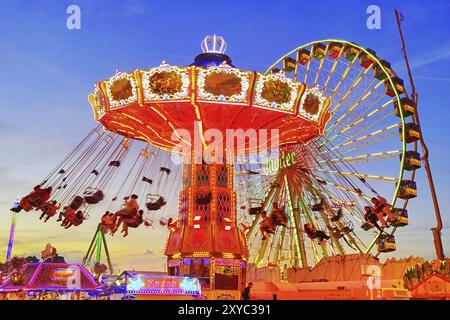La giostra a catena Wellenflug illuminata di colori e la ruota panoramica di sera, Cranger Kirmes, Herne, zona della Ruhr, Renania settentrionale-Vestfalia, G Foto Stock