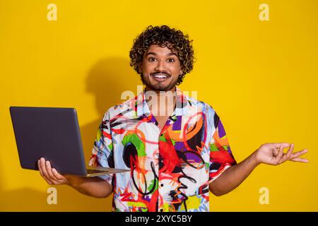 Foto di un giovane uomo gentile che tiene in mano il laptop indossa una camicia isolata su sfondo giallo Foto Stock