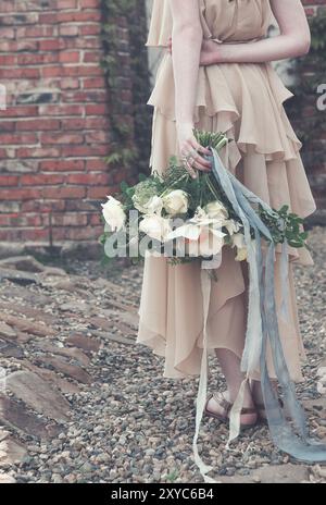 Crop donna indossa boho elegante abito rosa lungo e tenere bouquet meraviglioso con nastri sul molo nel parco Foto Stock