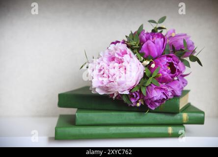 Bouquet nuziale di peonie rosa, tulipani e giglio della valle sui libri verdi Foto Stock