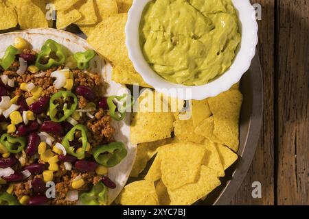 Tortilla messicana con carne, fagioli rossi, peperoncino jalapeno, nachos patatine e salsa guacamole visto da sopra Foto Stock