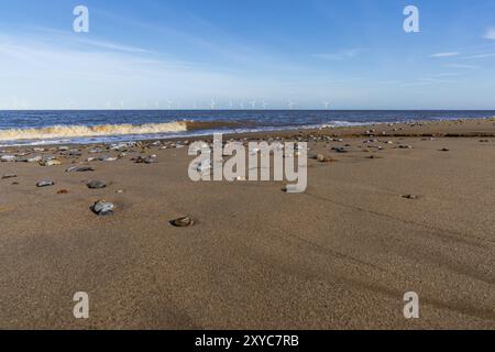 Costa del Mare del Nord a Caister-on-Sea, Norfolk, Inghilterra, Regno Unito, con un'onda che arriva in spiaggia e turbine eoliche sullo sfondo Foto Stock