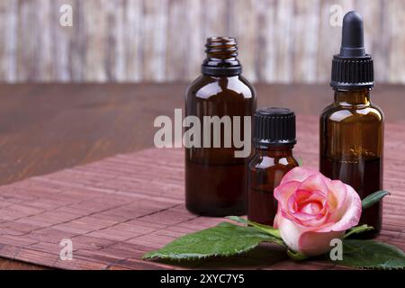 Bottiglie di olio essenziale rosa su sfondo marrone, focalizzazione selettiva Foto Stock