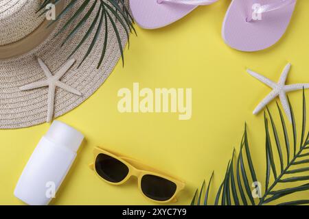 Accessori da spiaggia su sfondo giallo, occhiali da sole, crema solare, infradito e cappello, concetto di vacanza estiva, copia spazio Foto Stock