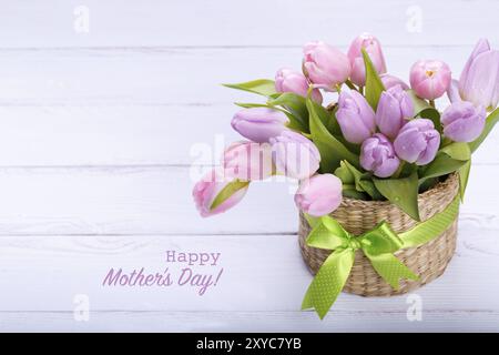 Bouquete di tulipani rosa in un cesto di vimini in bianco sullo sfondo di legno, con testo felice festa della mamma Foto Stock