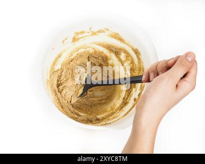 Persona che mescola un composto da forno in un recipiente di plastica bianco con una spatola nera verso il bianco Foto Stock