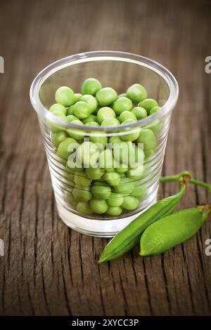 Piselli verdi freschi in un piccolo bicchiere sul tavolo rustico. Primo piano Foto Stock