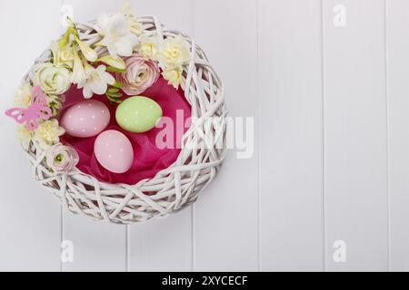 Cesto di uova di pasqua con fiori di colore bianco su sfondo di legno Foto Stock