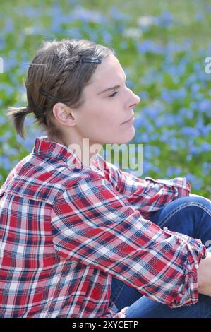Giovane donna attraente seduta in un prato con Scilla bifolia in primavera e godendo il sole. Giovane donna attraente seduta in un prato con SC Foto Stock
