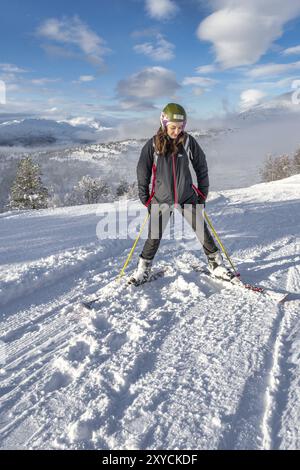 Donne con capelli marroni che fanno una pausa, sciando a stryn norvegia, in piedi fiduciosi sulla cima di una montagna, guardando giù, sorridente, orizzontale Foto Stock