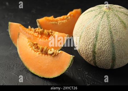 Meloni Cantaloupe maturi tagliati e interi su un tavolo con texture scura, primo piano Foto Stock