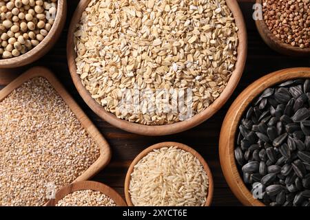 Diversi tipi di cereali, semi e legumi in ciotole su tavola di legno, piatti Foto Stock