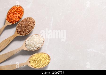 Diversi tipi di legumi e cereali in cucchiai di legno su tavolo in marmo chiaro, piatto. Spazio per il testo Foto Stock