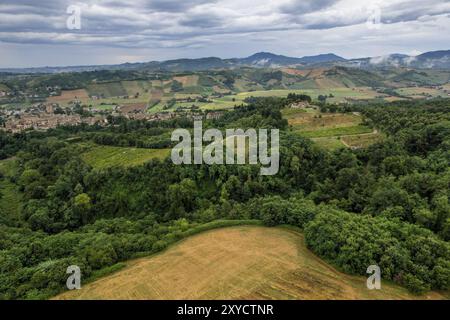 Vista aerea della campagna italiana che mostra verdi colline ondulate, terreni agricoli e un piccolo villaggio sotto un cielo nuvoloso. Castell'Arquato, Arda Valley, PC Foto Stock