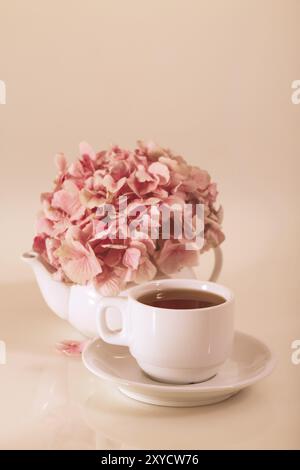 Teiera in porcellana e tazza per il tè con mazzo di petali di fiori rosa posti su sfondo beige Foto Stock