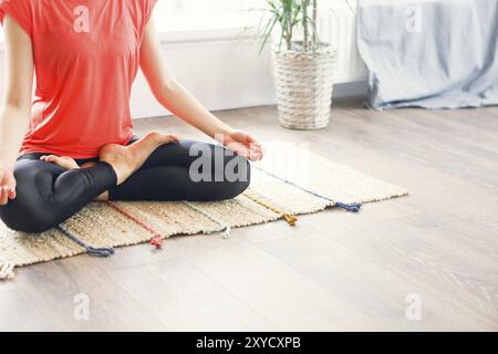 Attraente bruna giovane donna esercizio e seduta yoga in posizione del loto durante il riposo a casa Foto Stock