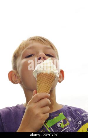 Il ragazzo mangia il gelato in giardino in estate. Bambino da otto anni. Blonder Junge mit Eis Foto Stock